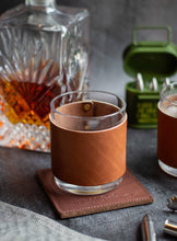 Load image into Gallery viewer, Glass with a leather sleeve on a coaster, surrounded by a decanter and other items.
