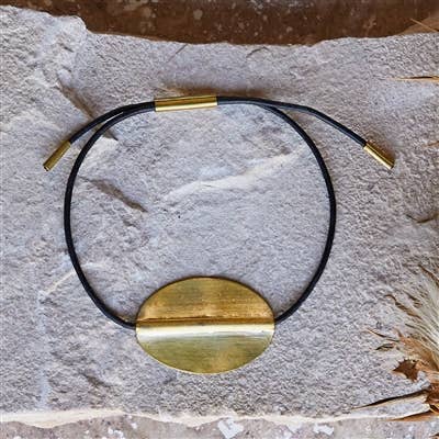 Black leather cord Bracelet with a gold pendant on a textured stone surface