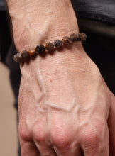Load image into Gallery viewer, A close-up of a person's hand and wrist wearing a beaded bracelet made of dark brown, black, and amber-brown polished stones.
