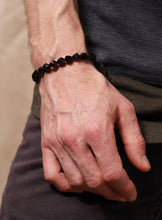 Load image into Gallery viewer, Hand wearing a black beaded bracelet with a blurred background
