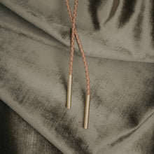 Load image into Gallery viewer, brass tails of a leather bolo tie on an olive green solk background
