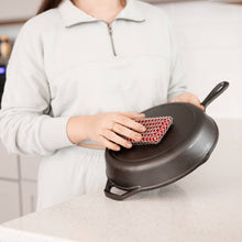 Load image into Gallery viewer, Person holding a black cast iron skillet with a red and white scrubber.
