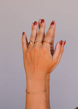 Load image into Gallery viewer, Hand wearing gold rings and a bracelet on a plain background
