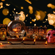 Load image into Gallery viewer, Glass decanter and skull-themed glasses on a wooden surface with warm lighting and decorative elements.
