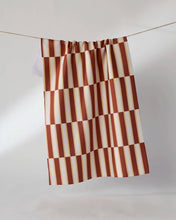 Load image into Gallery viewer, A curtain panel with a rust red and cream checkerboard pattern hanging from a thin wire against a light gray studio background.
