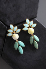 Load image into Gallery viewer, Pair of earrings with light blue floral tops and green leaves on a black stone
