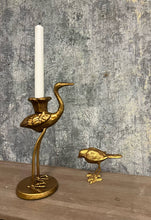 Load image into Gallery viewer, Gold crane candle holder with a candle on a wooden surface and textured wall background
