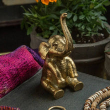 Load image into Gallery viewer, Gold elephant figurine on a surface with plants in the background
