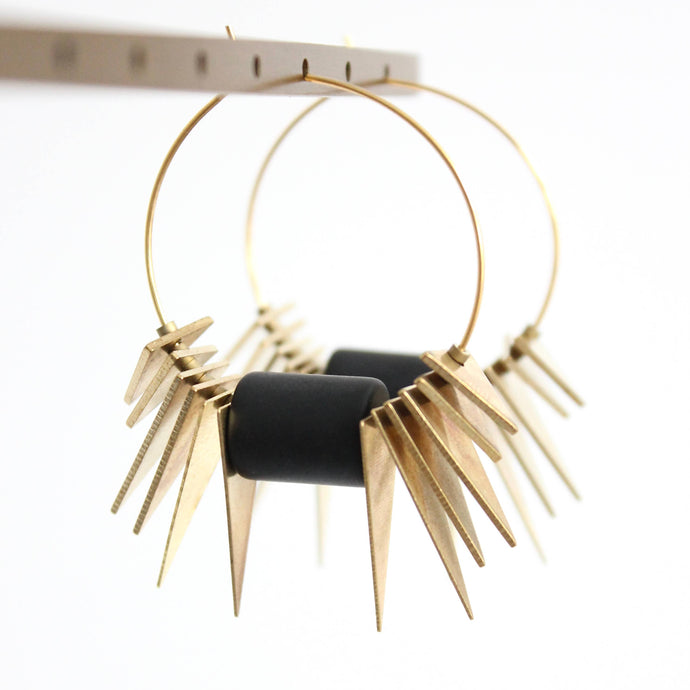 Gold earrings with spike-like designs and black central piece on a white background