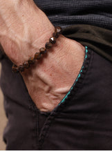 Load image into Gallery viewer, A close-up of a person's hand in a pocket wearing a dark brown faceted bead bracelet.
