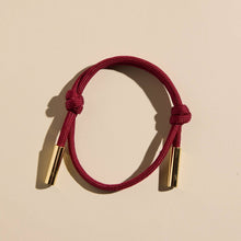 Load image into Gallery viewer, Red bracelet with gold ends on a beige background
