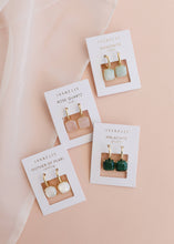 Load image into Gallery viewer, Three pairs of earrings on their packaging with a soft pink background
