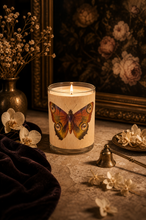 Load image into Gallery viewer, Candle with butterfly design in a decorative setting with flowers and a painting.
