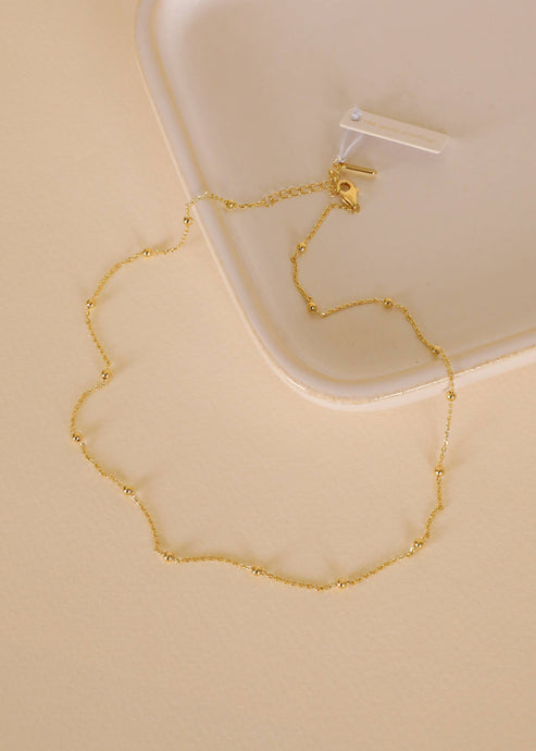 Gold necklace on a beige surface with a white container in the background