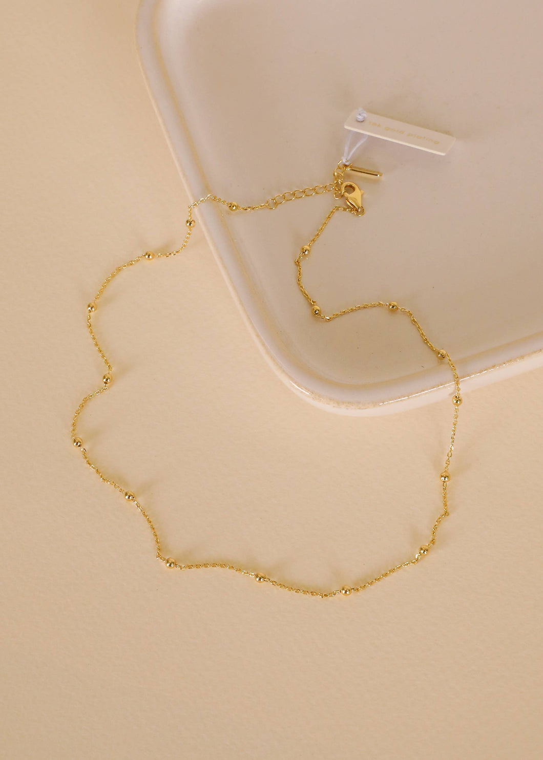 Gold necklace on a beige surface with a white container in the background