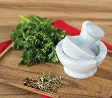 Load image into Gallery viewer, Marble mortar and pestle on a wooden surface with fresh herbs and spices.
