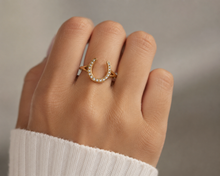 Load image into Gallery viewer, Gold horseshoe ring with small diamonds on a hand against a neutral background
