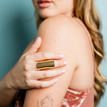 Load image into Gallery viewer, Woman with a gold ring on her hand touching her shoulder against a blue background
