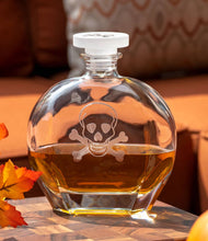 Load image into Gallery viewer, Glass decanter with skull and crossbones design on a wooden surface with autumn leaves and pumpkins.

