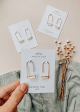 Load image into Gallery viewer, Gold earrings on a card held by a hand with a neutral background

