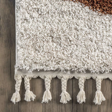 Load image into Gallery viewer, Close-up of a textured rug with braided tassels on a wooden floor.
