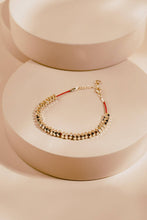 Load image into Gallery viewer, Gold bracelet with red string on a beige stand
