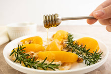 Load image into Gallery viewer, Honey being drizzled over a dish of yellow food with rosemary on a white plate.
