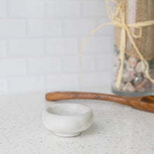 Load image into Gallery viewer, White marble bowl on a speckled countertop with a wooden spoon and jar in the background.
