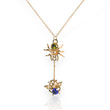 Load image into Gallery viewer, A gold-tone spider and bee pendant necklace on a delicate chain, featuring a green stone, a white pearl, and a blue stone on a clean white background.
