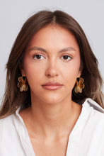 Load image into Gallery viewer, Woman wearing gold flower earrings against a plain background
