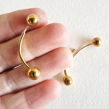 Load image into Gallery viewer, Hand holding an Arc ball stud Earrings in polished brass on a white background
