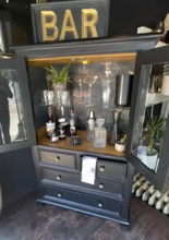 Load image into Gallery viewer, Dark wooden bar cabinet with open doors displaying bar equipment and decor.
