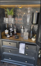 Load image into Gallery viewer, Dark wooden bar cabinet with liquor bottles, glasses, and decorative items.
