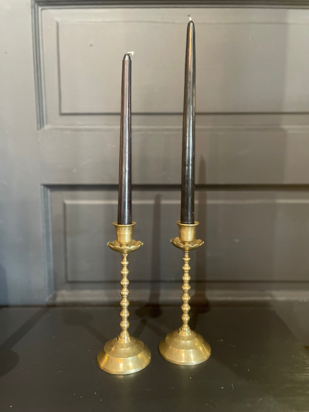 Two tall candlesticks with brass bases and black candles on a dark surface.