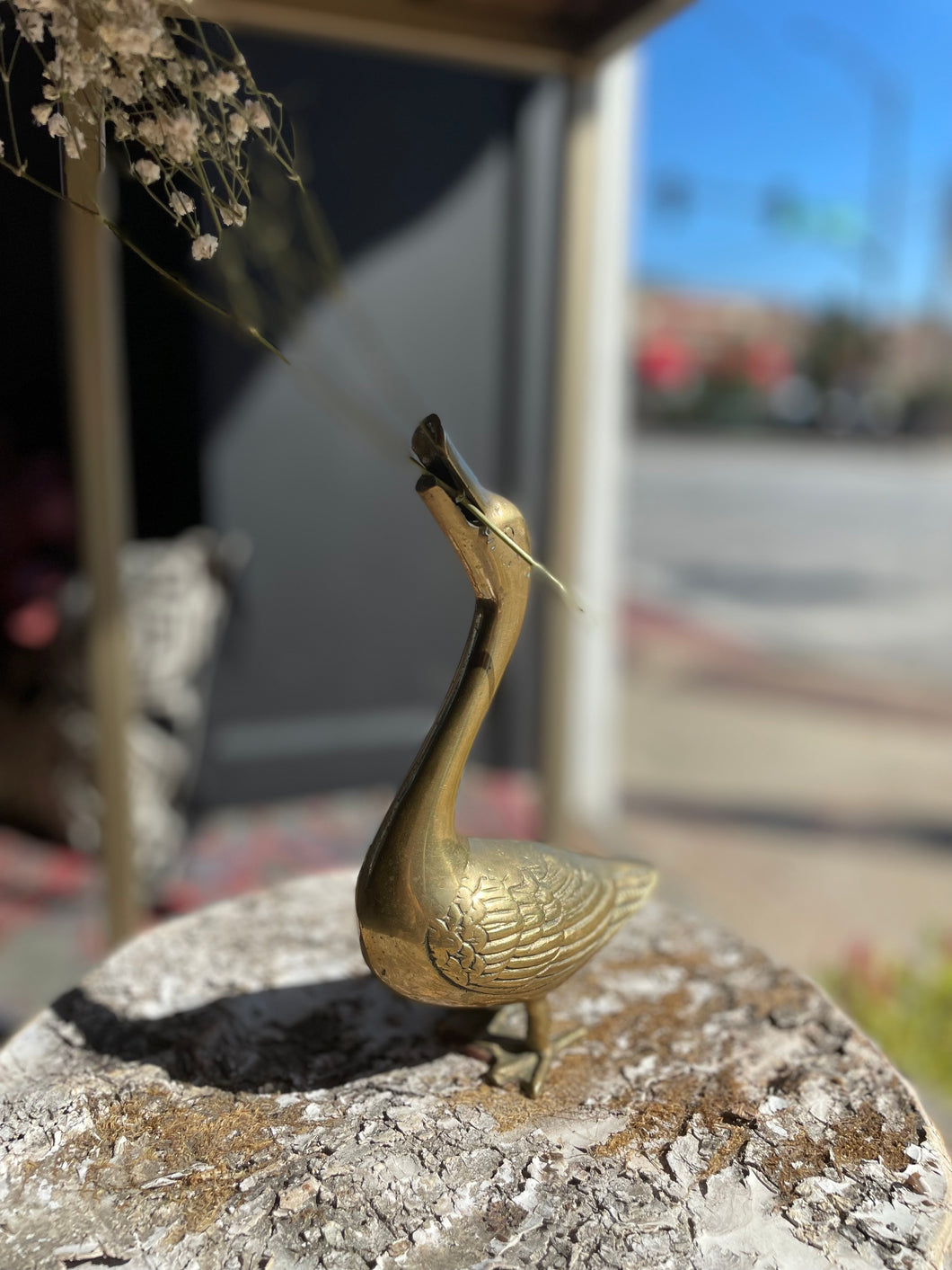 Brass goose figurine on a stone surface with a blurred outdoor background