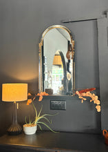 Load image into Gallery viewer, Decorative mirror with gold frame on a dark wall next to a lamp and small plant.
