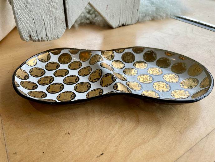 Divided glass dish with gold and black medallion motif on a wooden surface