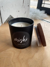 Load image into Gallery viewer, Black candle in a container with 'mishi' branding on a wooden surface
