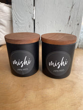 Load image into Gallery viewer, Two black candles with wooden lids on a wooden surface.
