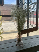 Load image into Gallery viewer, Clear vase with dried flowers on a wooden surface near a glass door.
