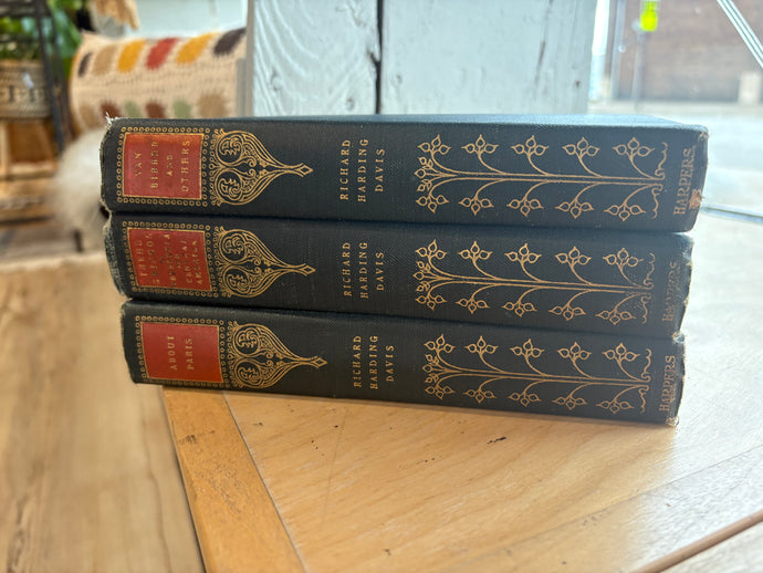 Three books stacked on a wooden surface with decorative spines.