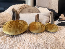 Load image into Gallery viewer, Three velvet decorative pumpkins in shades of mustard yellow and olive gold, arranged on a chunky knit beige throw blanket in a cozy living room setting.
