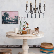 Load image into Gallery viewer, Round marble table with decorative items in a room with a chandelier and wall art.
