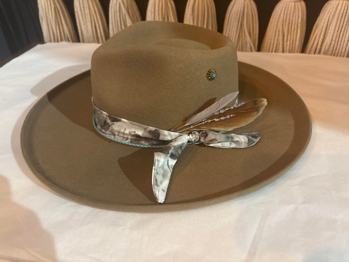 Brown hat with a decorative band featuring feathers on a white surface.