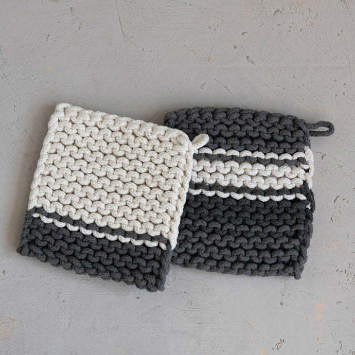 Two knitted pot holders, one white and gray, the other black and gray, on a light gray surface.