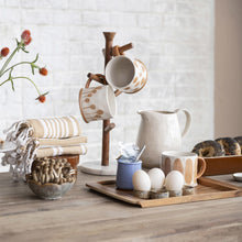 Load image into Gallery viewer, Kitchen counter with mugs, eggs, and a pitcher on a wooden surface.
