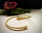 Assymetrical wrap bracelet in brass displayed with a floral arrangement