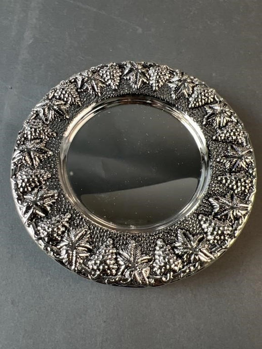 Round metallic mirror with intricate designs on a gray background