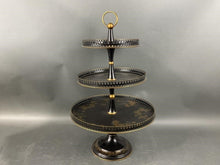 Load image into Gallery viewer, Three-tiered decorative stand with black and gold  and floral design on a gray background
