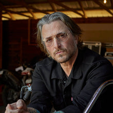 Load image into Gallery viewer, Man with glasses and a beard sitting in a dimly lit room.
